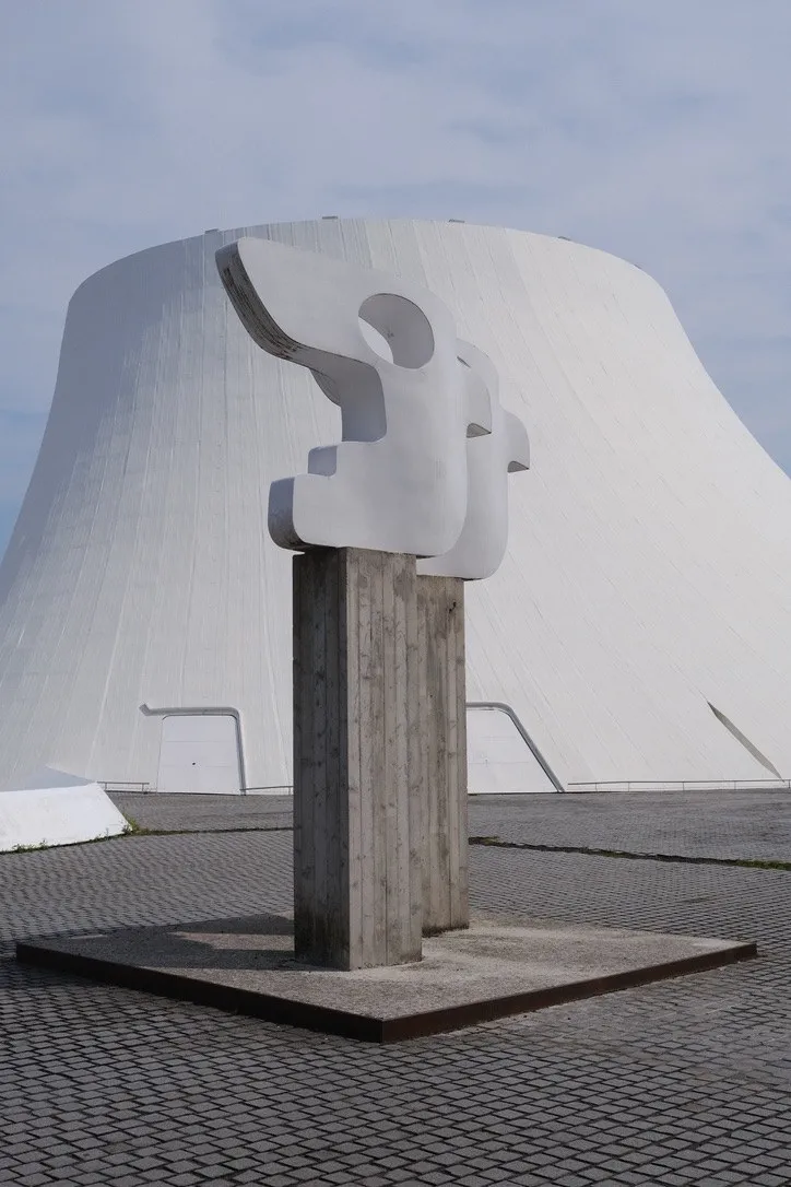 A white abstract sculpture in front of a curved concrete building