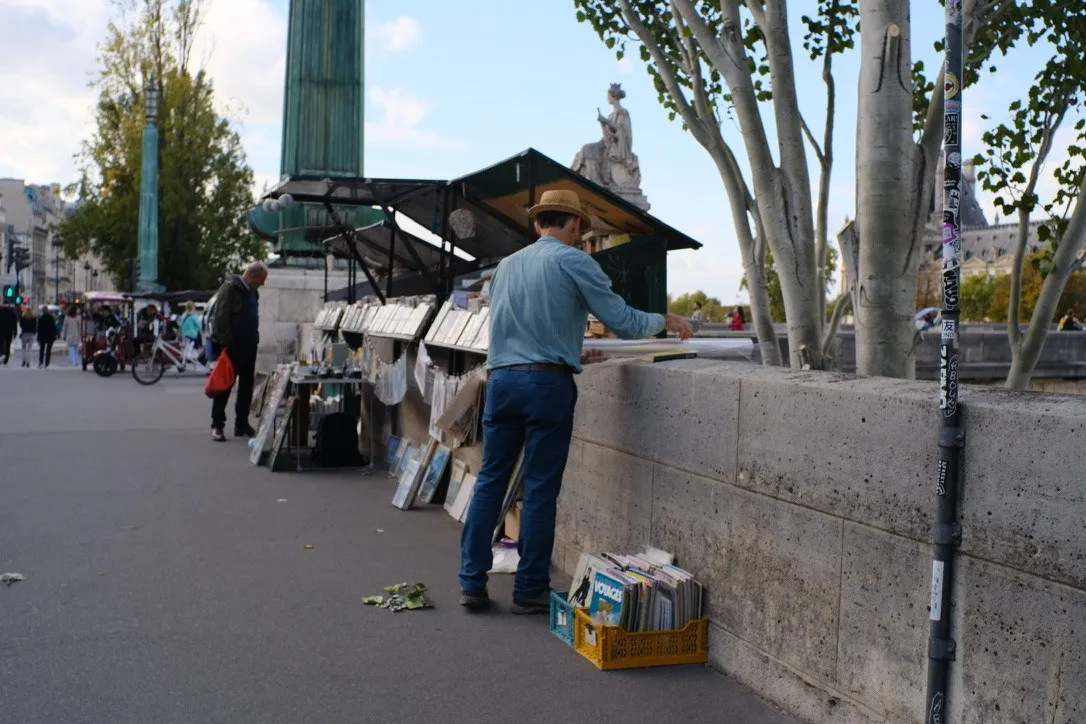 A bookseller arranging books along a tree-lined riverside