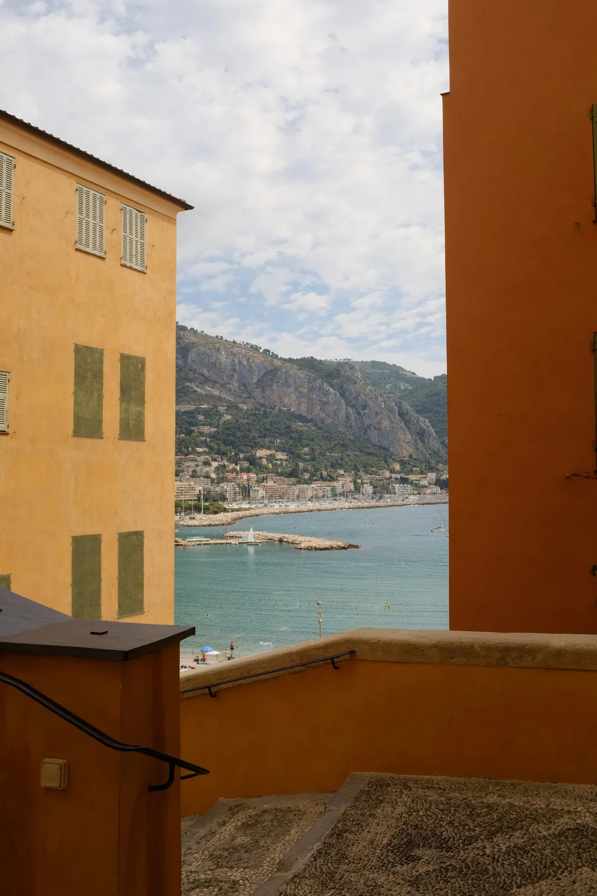 Ochre buildings framing a view of the coast from a staircase