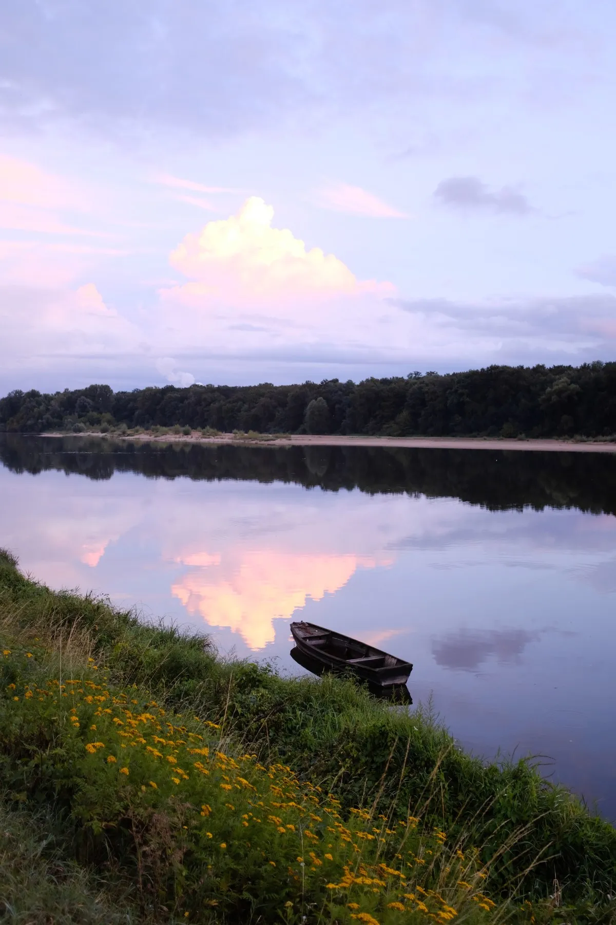 A small boat beside a still lake reflecting pink evening clouds