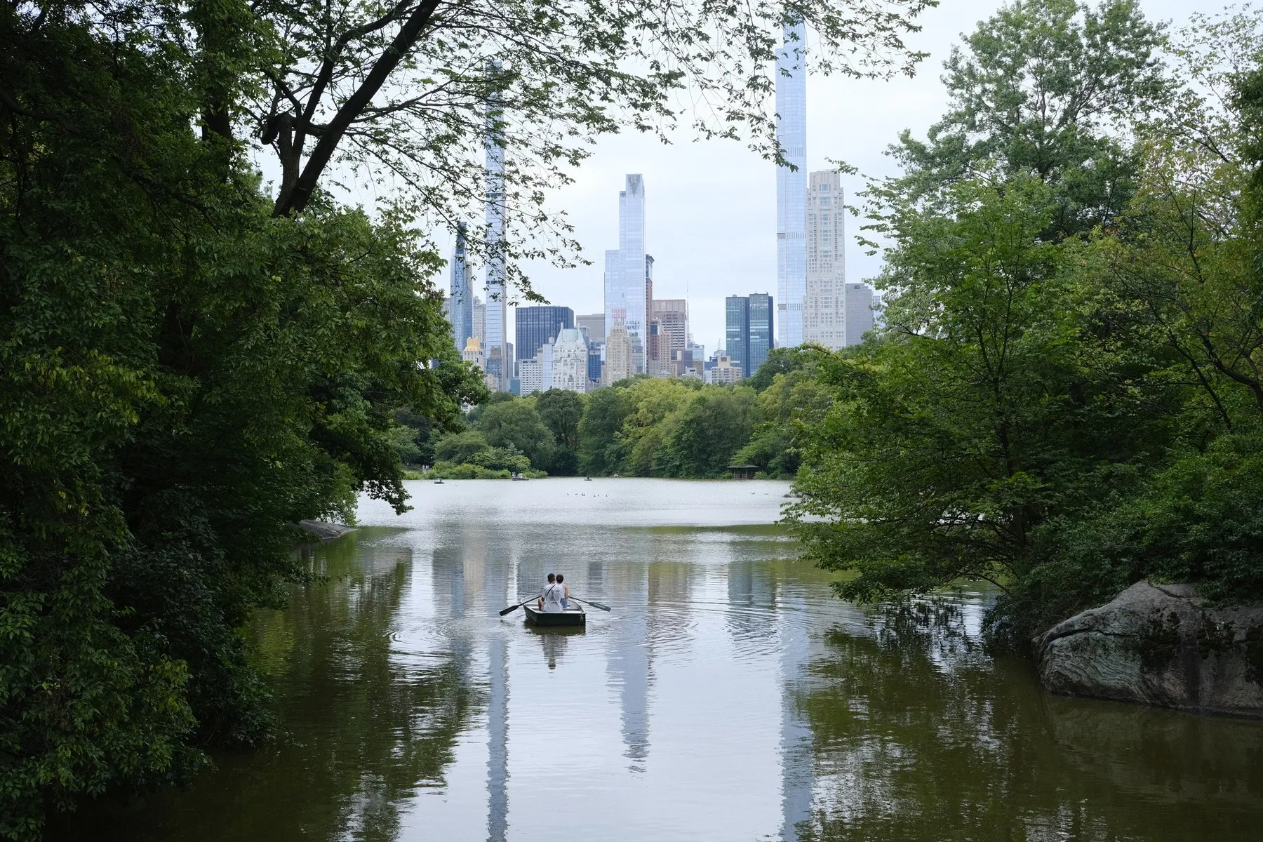 A rowboat on a lake framed by trees and the city skyline